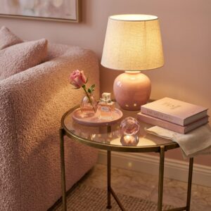 Close-up styling vignette of a gold and glass round living room side table styled with an amber ceramic lamp, pink crystal object, and design books.