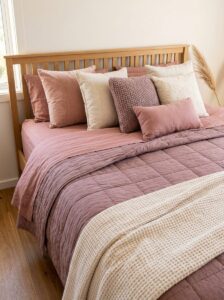 Cozy pink bedroom bedding with layered textures including a dusty rose waffle-weave duvet, ivory linen sheets, and a cream chunky knit blanket.