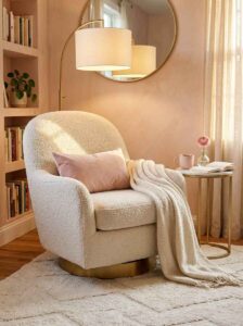 A bright Pinterest-worthy cozy reading nook aesthetic featuring a deep cream boucle chair, white built-in shelves with color-coded pink books, and gold decor accents.