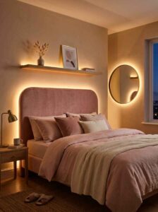 Modern pink LED bedroom aesthetic with hidden warm-white LED strip accent lighting creating a soft glowing halo behind a velvet bed headboard and round mirror.