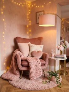 Cozy bedroom reading nook corner ideas featuring a plush dusty pink velvet armchair, a chunky pink knit throw blanket, a marble side table with coffee, a gold arched floor lamp, and a small pink shag rug.