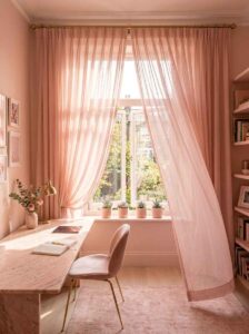 Blush pink office window styled with flowing sheer curtains, natural sunlight streaming over a marble desk, pink velvet chair, and area rug.