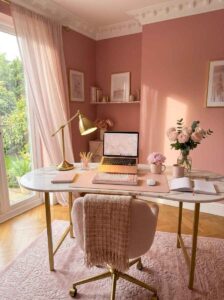Bright feminine desk setup featuring cozy home office ideas with a marble top, gold desk lamp, pink keyboard, and fresh roses in warm sunlight.