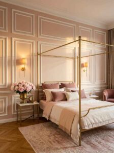 A cohesively decorated soft pink bedroom showing white board and batten molding, a brass canopy bed, warm sconces, and layered bedding.