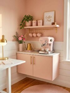 Cozy blush pink home office coffee station corner featuring a pink espresso machine, gold hardware cabinets, wall shelves, and a coffee mugs setup.