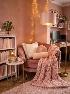 Cozy home office reading nook featuring a tufted blush velvet armchair, chunky knit throw blanket, floor lamp, and side table with books.