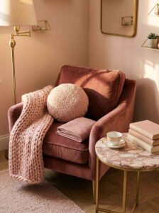 A luxurious reading corner bedroom design styling a mauve velvet armchair with a round sherpa pillow, a pink marble accent table, and an oak floor frame.