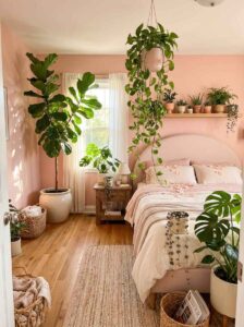 Urban jungle small bedroom aesthetic with multiple indoor plants, a tall fiddle leaf fig plant in a white ceramic pot, a hanging devil’s ivy vine, and wood floating shelves over a pink headboard.