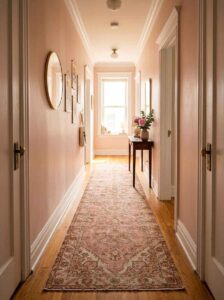 A long narrow hallway featuring a vintage blush pink runner rug on light oak hardwood floors for warm, cozy entryway decor.
