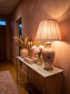 A modern entryway decor setup showcasing a patterned ceramic table lamp emitting soft, warm lighting next to fresh pink flowers on a marble console table.