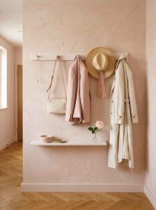Minimalist wooden wall hooks holding a trench coat, straw hat, and woven tote bag for renter-friendly, welcoming entryway ideas.